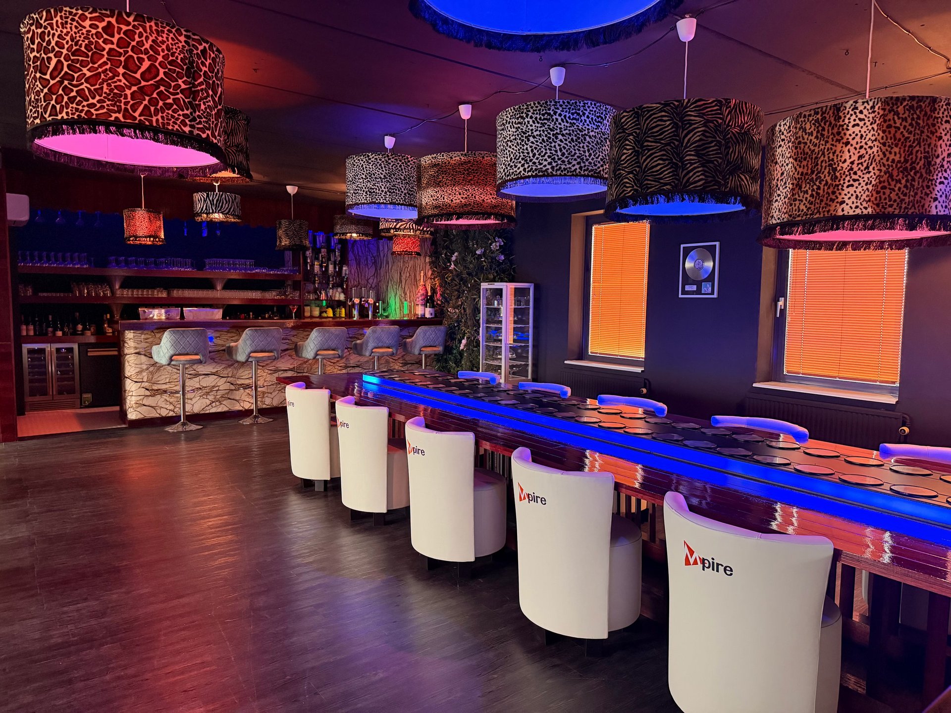 Modern nightclub interior with illuminated cylindrical white counter, colorful ambient lighting, and textured decorative ceiling elements