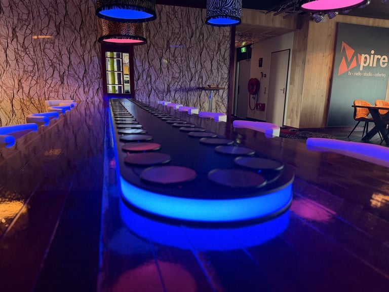Modern indoor space with neon blue and pink lighting, featuring curved glowing platforms and textured walls in a futuristic lounge or entertainment venue